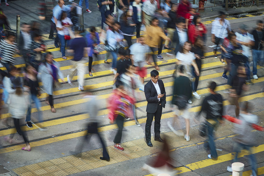 Busy man on smartphone surrounded by people rushing across a city crosswalk.