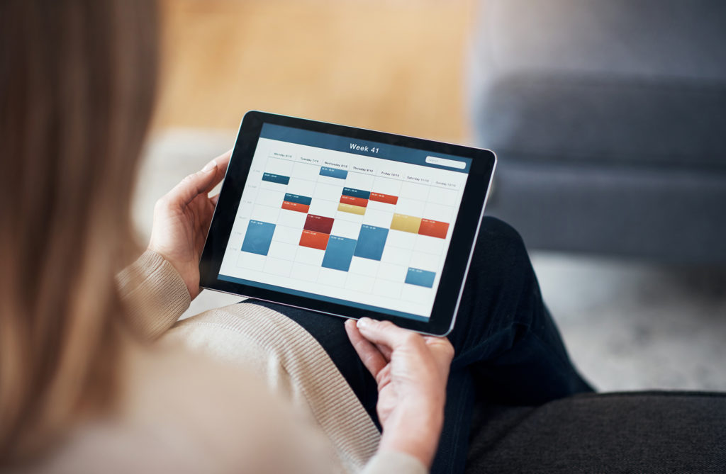 A woman sitting and viewing a timetable on a tablet in her living room.