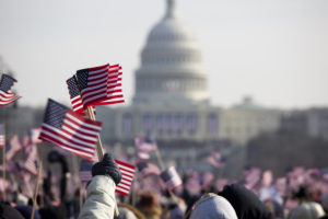 People wave American flags in a crowd standing in front of the U.S. Capitol building.